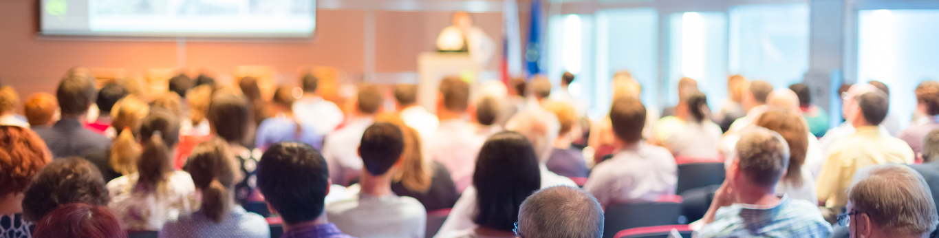 A crowd of seated conference attendees listening to a presenter on stage