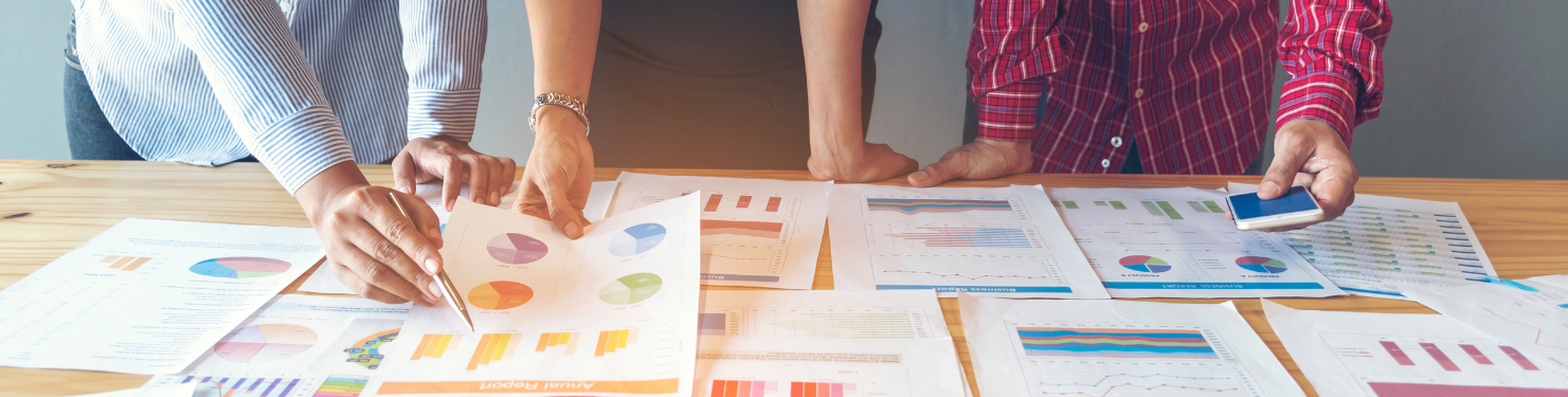 Three people referring to post-event reporting data that has been printed out and displayed on a table